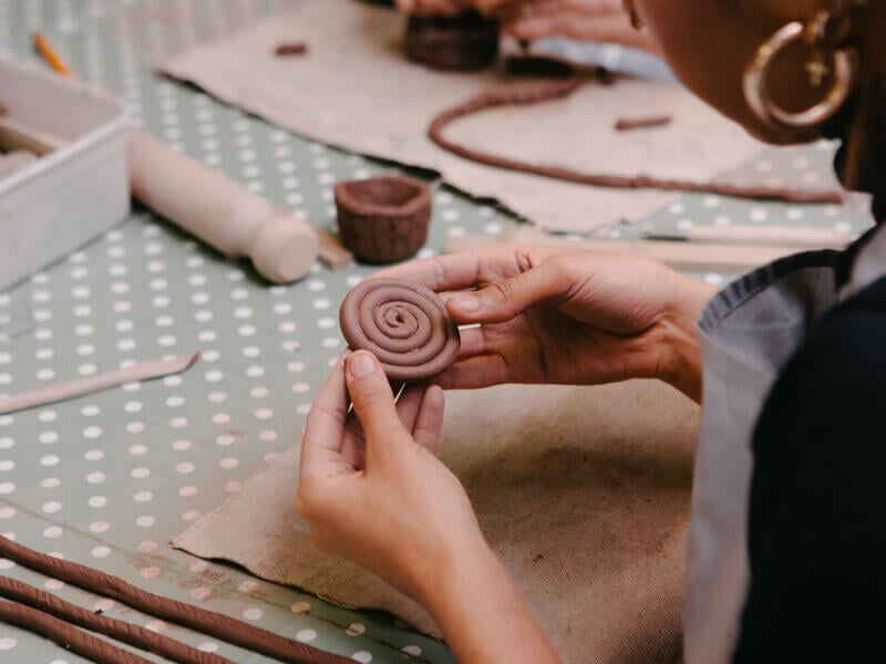 Woman holding a coiled piece of clay over a workbench